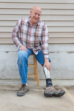 Amputee Man On A Stool Looking Forward Reaching Down To Adjust Prosthetic Leg, Copy Space, Vertical Aspect