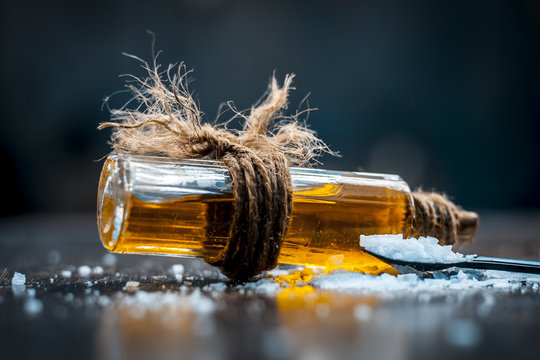Close up of aurvedic herb camphor powder in a small spoon and its oil on brown wooden surface in dark Gothic colors is helps in Prevents Skin Infections,Eliminates Gas,Reduces Nervous Disorders etc.