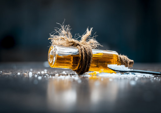 Close up of aurvedic herb camphor powder in a small spoon and its oil on brown wooden surface in dark Gothic colors is helps in Prevents Skin Infections,Eliminates Gas,Reduces Nervous Disorders etc.