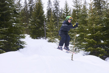 Little boy jumping on downhill skis in forest. Skiing between trees. Adrenaline sport in winter
