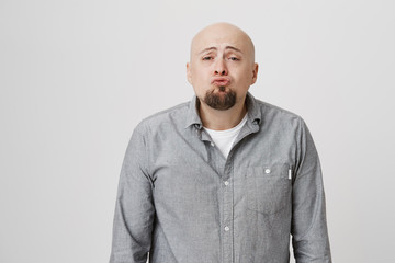 Young funny bearded man folding his lips to kiss with puppy look in his eyes over white background. Adult guy in casual gray shirt standing in front of his lover ready to receive kiss