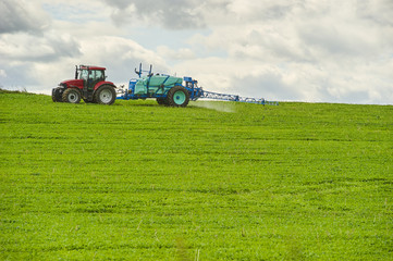 Obraz premium Tractor spraying pesticides on field with sprayer at spring