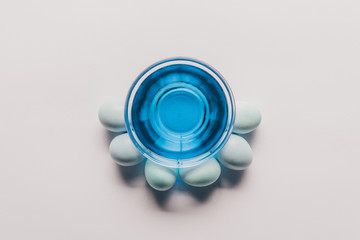 Top view of glass with blue paint and chicken eggs on white surface, easter concept