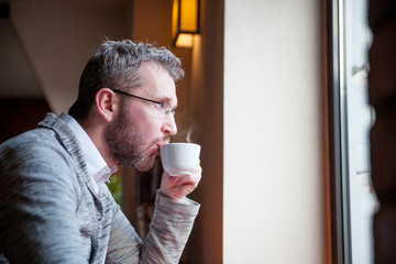 Thoughtful man drinking coffee in cafe and looking out window