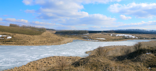 Springtime.Sunny spring colorful landscape with river and trees growing on the riverbank.Melting ice and snow.Clouds in blue sky.Beautiful view. 