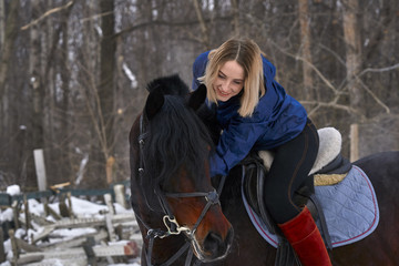 A young girl with white hair is riding a horse. The girl hugs her favorite horse. Winter cloudy...