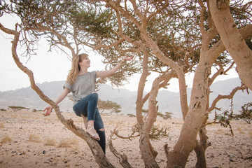 Pretty girl have fun on a tree in the desert