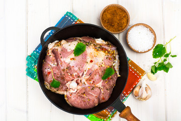 Frying pan with piece of raw meat with spices on white wooden table