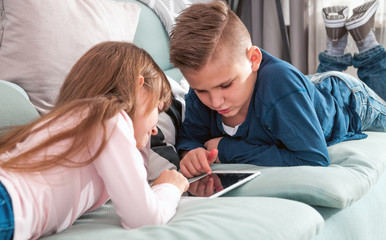Obraz premium Happy children on sofa at home playing with digital tablet together
