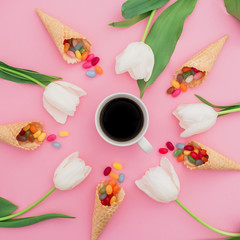 Obraz na płótnie Canvas Composition of colorful bright candy in waffle cones, cup of coffee and white flowers on pink background. Flat lay, top view