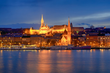 Illuminated St. Matthias church and Szilágyi Dezső cathedral across Danube river at night, Budapest