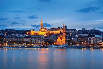 Illuminated St. Matthias church and Szilágyi Dezső cathedral across Danube river at night, Budapest