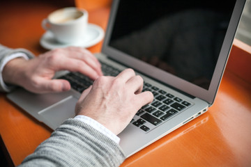 Cropped image man typing on laptop keyboard in the cafe
