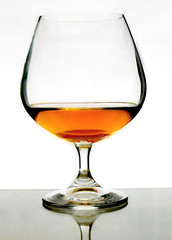 A brandy snifter filled with brandy or cognac sitting on a reflective grey surface with bright...