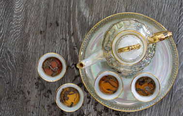 Chinese teapot set with cup which has hot tea in tray and dry tea leaf all on the plank