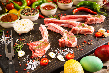 Raw lamb ribs preparation on rustic cutting board - Fresh chops of meat with colorful spices and vegetables background - Easter holidays food concept