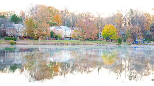 Timelapse, time lapse of sunrise on Braddock lake in Burke, Virginia, USA, Fairfax county with reflection of townhouses, fog, mist floating above on water surface in autumn, fall and orange trees