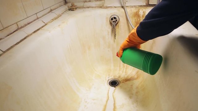 A man's hand in orange rubber gloves pours a gel into the sink to clean or wash the tub and toilet in the bathroom. General house cleaning.