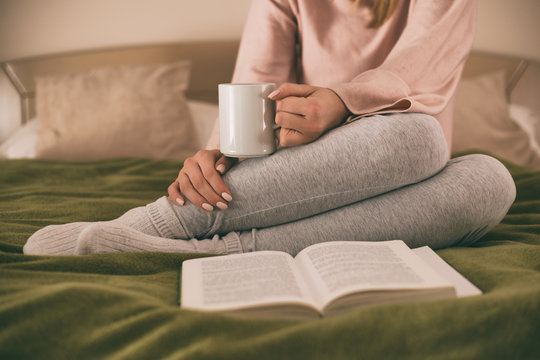 Photo of woman relaxing while reading a book and drinking coffee.