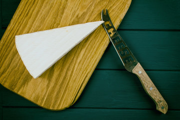 A piece of brie cheese with a knife on a wooden  background