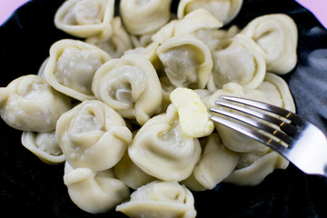 Boiled dumplings on a black plate on a pink wooden background.