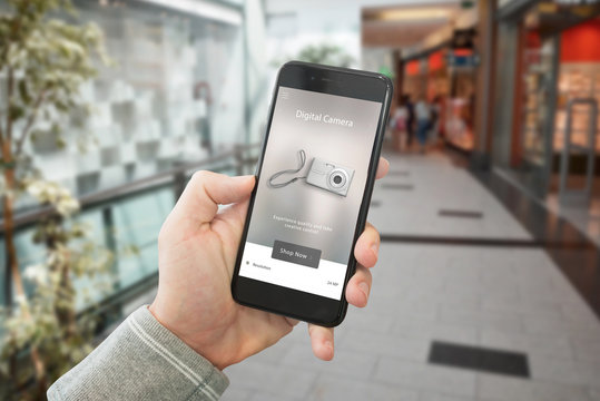 Shopping technological products with web site on smart phone display. Shopping mall in background.