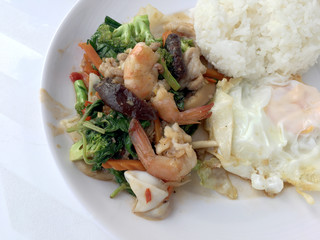 Vegetable stir-fry dish with Thai healthy food stir-fried broccoli, mushroom, carrot, hearb, squid and shrimp with rice and fried egg in white plate on white background.  Thai style fast food can orde