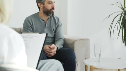 Tilt up of Angry man talking about his family porblems with female psychologist in her office indoors