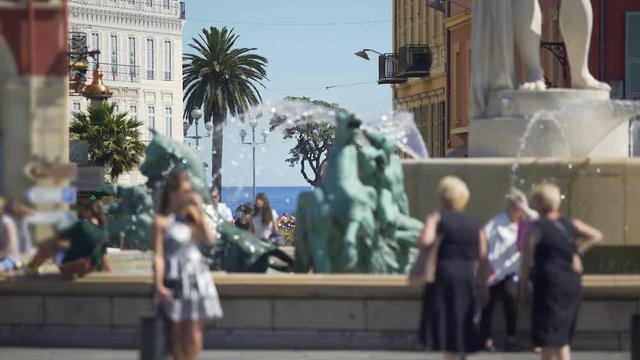 People walking by and taking pictures near Sun Fountain in Nice, city life