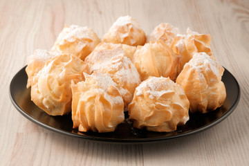 Eclairs of homemade baking in black plate on a wooden table closeup. Unhealhy food for your figure.