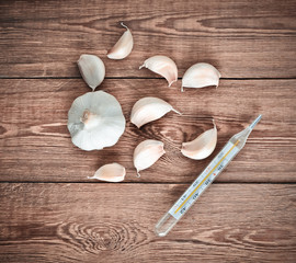 Garlic cloves and thermometer on a wooden table. Traditional medicine against colds..