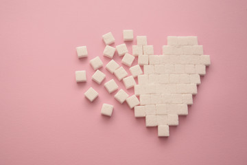 Broken heart made of sugar cubes. Rupture of relations. Sugar kills. Pink background.