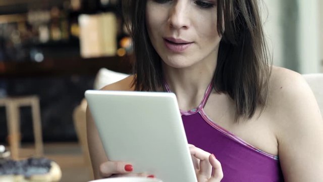 Happy, pretty woman using tablet and drinking coffee in cafe
