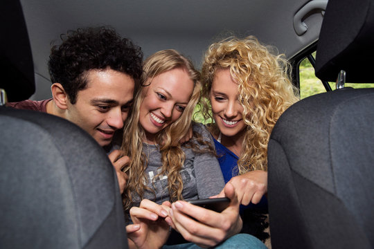 Friends in back seat of car looking at smartphone