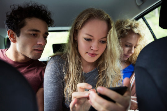 Friends in back seat of car looking at smartphone