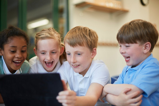 Schoolboys and girls laughing at digital tablet in classroom at primary school
