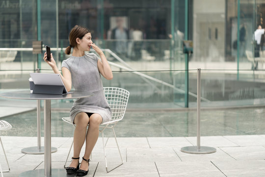 Young city businesswoman at sidewalk cafe holding up smartphone