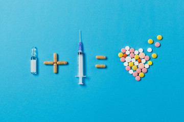 Pills ampoule plus empty syringe needle equals medication colorful round tablets in form of heart isolated on blue background. Concept of treatment, choice healthy lifestyle. Copy space advertisement.