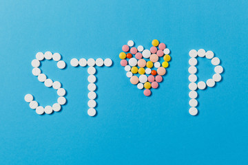 Medication white, colorful round tablets in word Stop isolated on blue background. Pills heart shape, form, letter. Concept of health, treatment, choice, healthy lifestyle. Copy space advertisement.