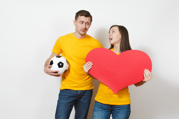 Sad upset young couple, woman, man, football fans with soccer ball, big red heart cheer up team worries about losing team isolated on white background. Sport, family, lifestyle concept. Copy space.