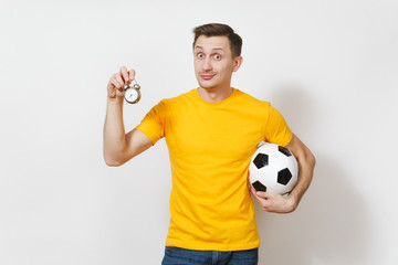 Inspired young cheerful European man, fan or player in yellow uniform hold soccer ball, old alarm clock, cheer favorite team isolated on white background. Sport, play football, lifestyle concept.