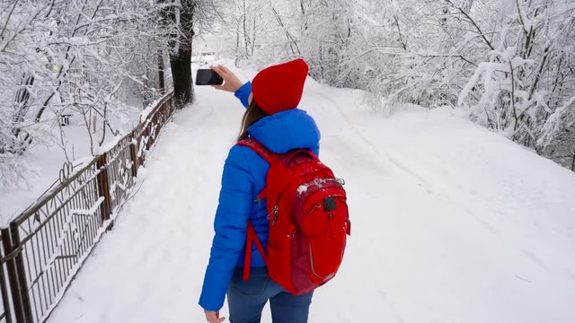 Young woman uses a smartphone for make a photos of a beautiful winter snow-covered landscape