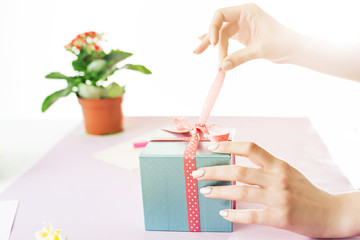 Close-up of female hands holding a present. The trendy pink desk.