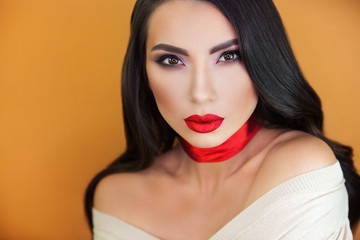 a beautiful girl with sensual bright red lips on an orange background, a red ribbon on her throat does not leave anyone indifferent, everyone looking into her brown eyes.