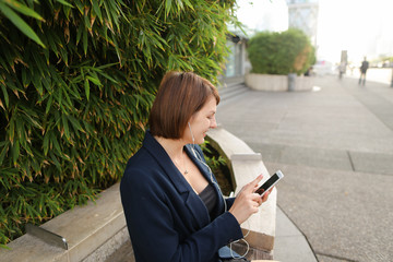 Businesswoman listening to music and chatting with smartphone and in ear phones outside. Concept of...