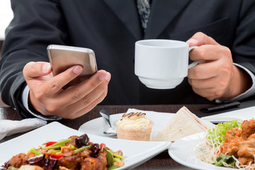 Close up of Businessman checking the news from mobile phone and taking coffee cup while eating...
