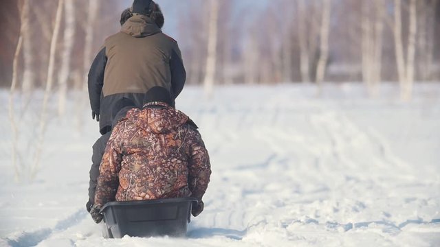 Three men in winter clothes riding through the winter field on a mini snowmobile with a trailer