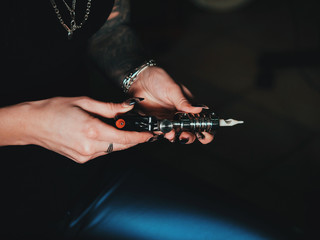 Artist prepares tools and machine for tattoo session, woman holding a tattoo gun. The tattooist...