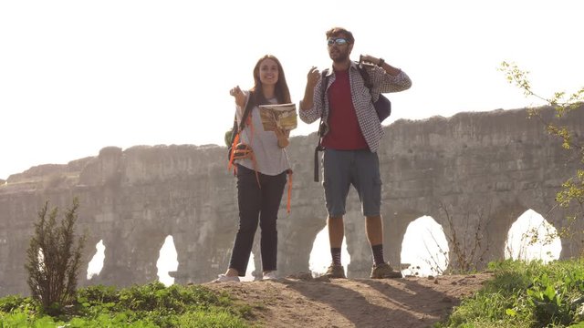 Young lovely couple backpackers tourists reading map pointing directions roman aqueduct arches in parco degli acquedotti park ruins in rome on romantic misty sunrise with guitar and sleeping bag slow