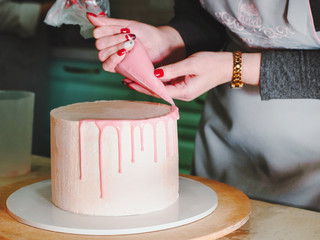 Unrecognisable woman decorating mousse glaze cake with rose, macarons, hands detail, focus on the...